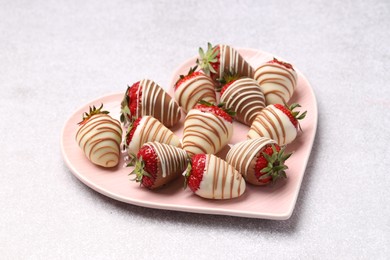 Photo of Heart shaped plate with delicious chocolate covered strawberries on light table