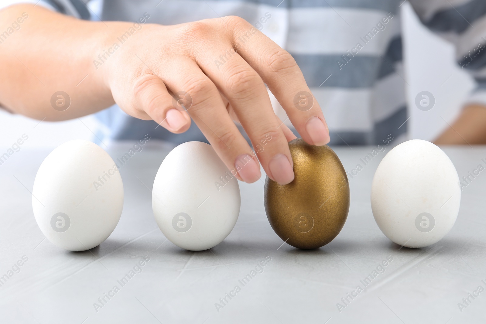 Photo of Woman choosing golden egg from white ones at table, closeup