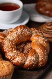 Photo of Freshly baked round braided bread and other pastries on wooden board, closeup