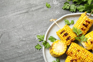 Delicious grilled corn cobs on grey table, flat lay. Space for text