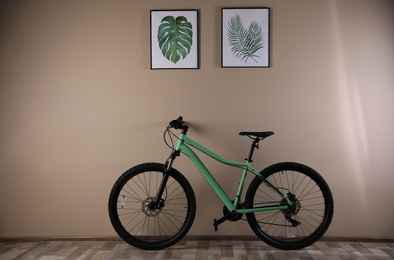 Modern green bicycle near beige wall indoors