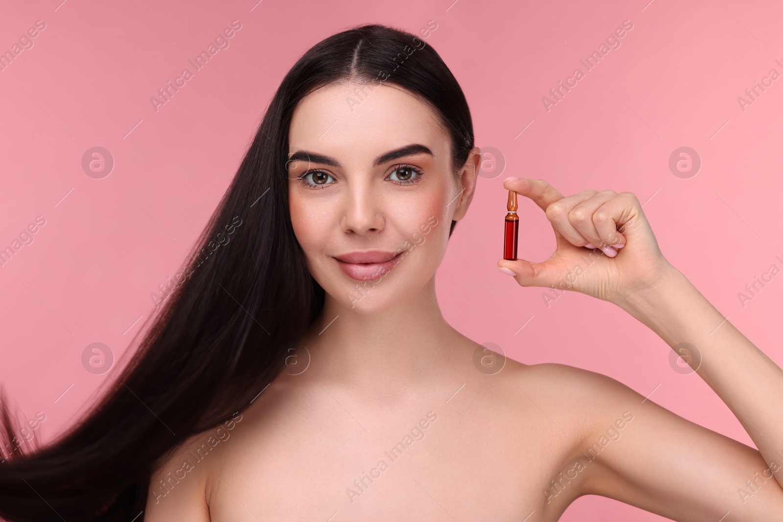 Photo of Beautiful young woman with long healthy hair holding ampoule on pink background