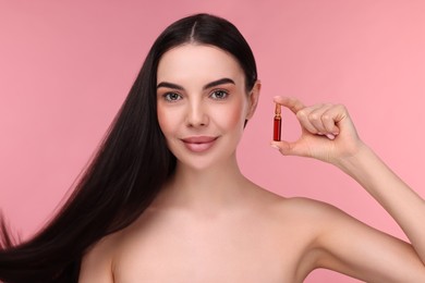 Photo of Beautiful young woman with long healthy hair holding ampoule on pink background