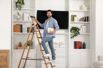Photo of Happy man with books on wooden folding ladder at home