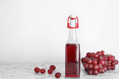 Photo of Bottle with wine vinegar and fresh grapes on marble table. Space for text