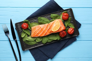 Photo of Tasty grilled salmon with tomatoes, spinach and lemon served on light blue wooden table, top view