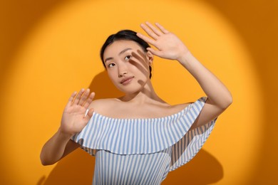 Photo of Beautiful young woman shading herself with hand from sunlight on orange background