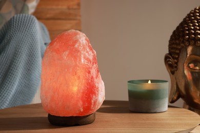 Beautiful Himalayan salt lamp and candle on wooden table indoors
