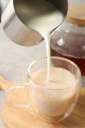 Photo of Pouring milk into glass cup with tea at table, closeup