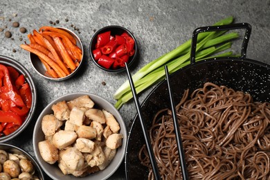 Wok with noodles, chicken and other products on grey table, flat lay