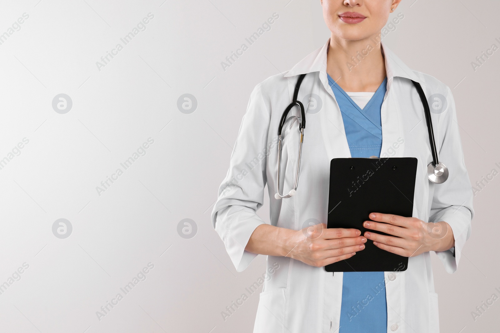 Photo of Doctor with stethoscope and clipboard on light grey background, closeup. Space for text