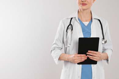 Photo of Doctor with stethoscope and clipboard on light grey background, closeup. Space for text