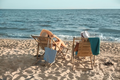 Photo of Young couple relaxing in deck chairs on beach near sea