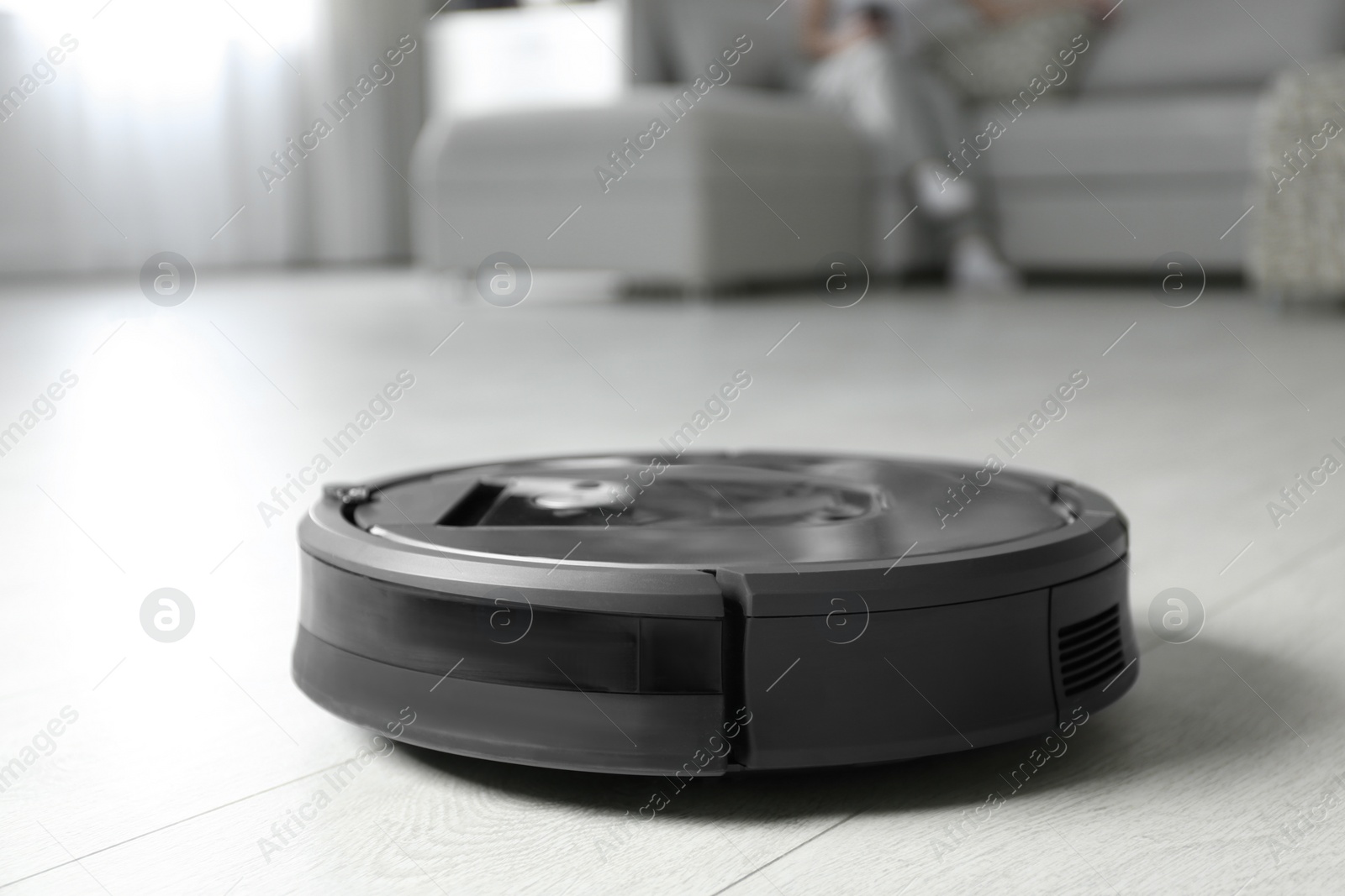 Photo of Modern robotic vacuum cleaner and blurred woman resting on background