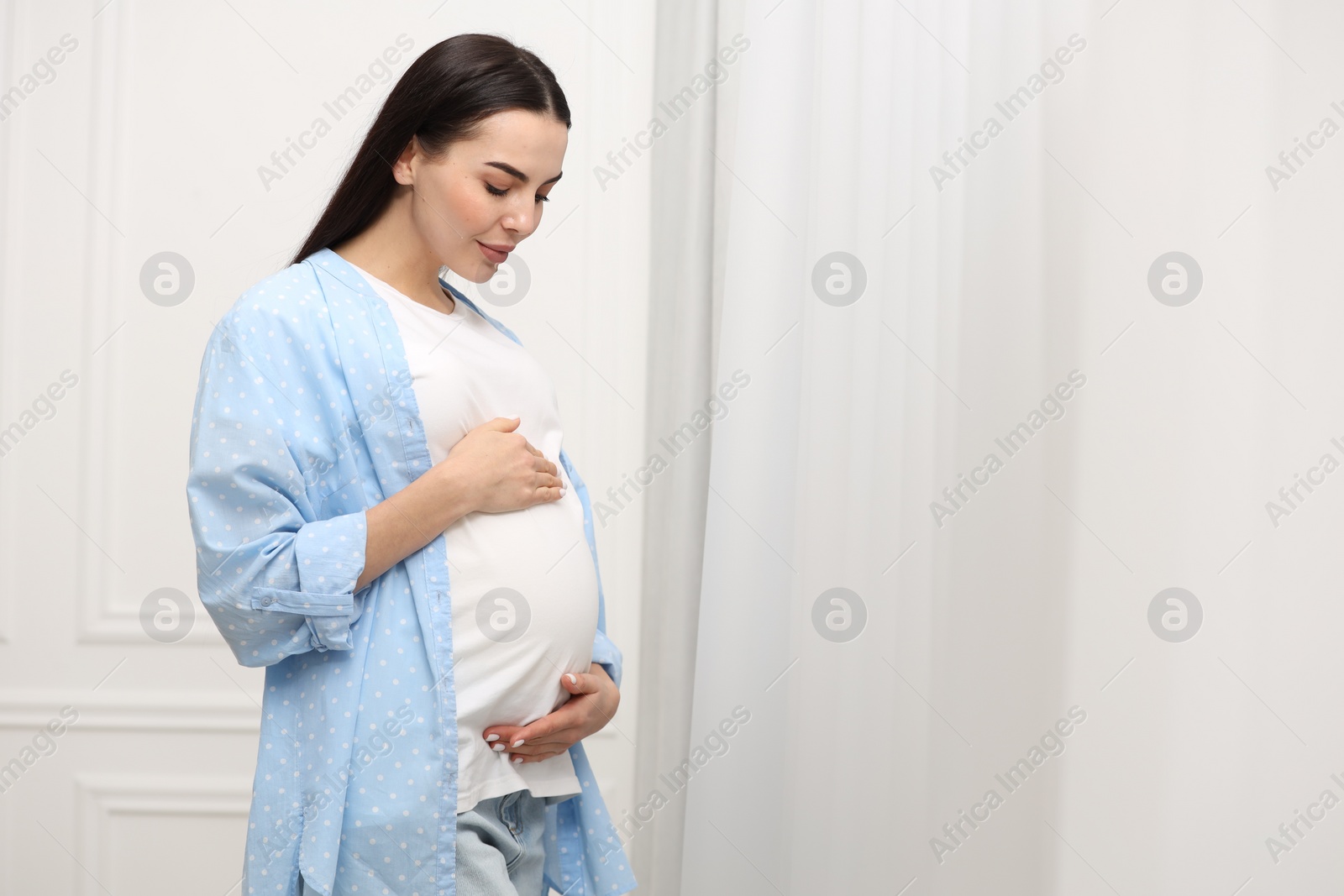 Photo of Pregnant young woman near window indoors, space for text