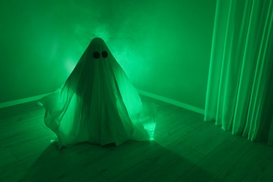 Photo of Creepy ghost. Woman covered with sheet in green light, space for text