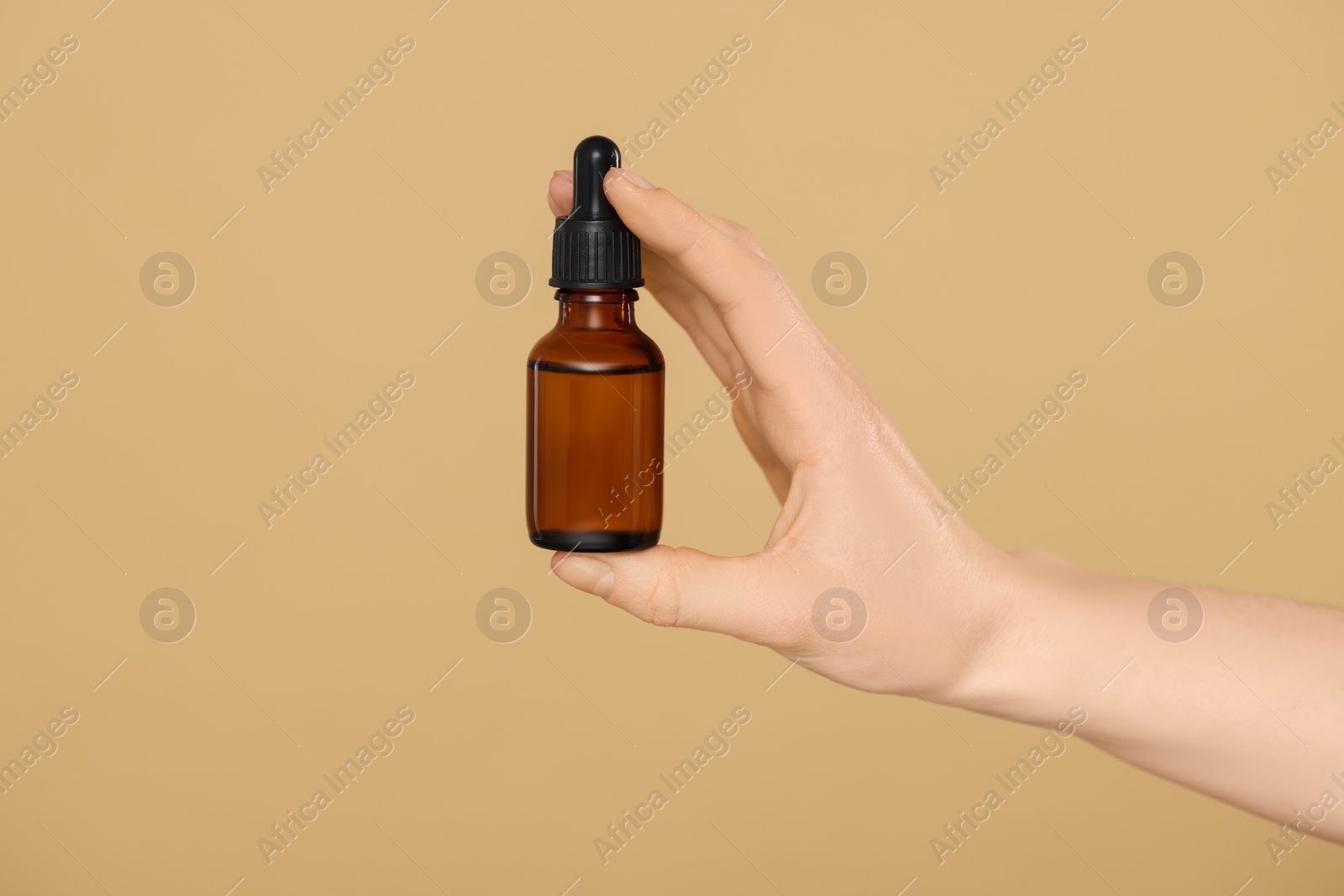 Photo of Woman holding bottle of essential oil on beige background, closeup