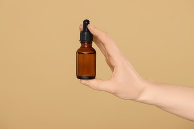 Photo of Woman holding bottle of essential oil on beige background, closeup