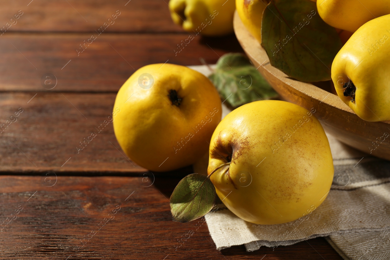 Photo of Tasty ripe quince fruits in bowl on wooden table, closeup. Space for text