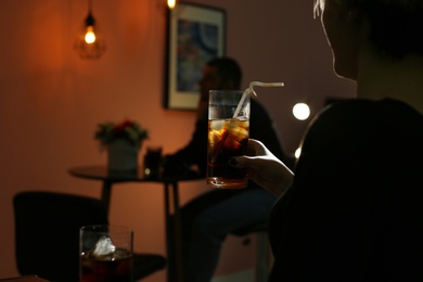 Woman with glass of cold cola in dark cafe, closeup. Space for text