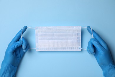 Doctor with protective mask on light blue background, top view. Safety equipment