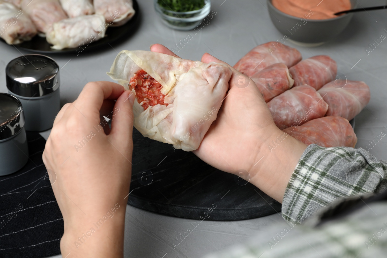 Photo of Woman making stuffed cabbage rolls at grey table, closeup