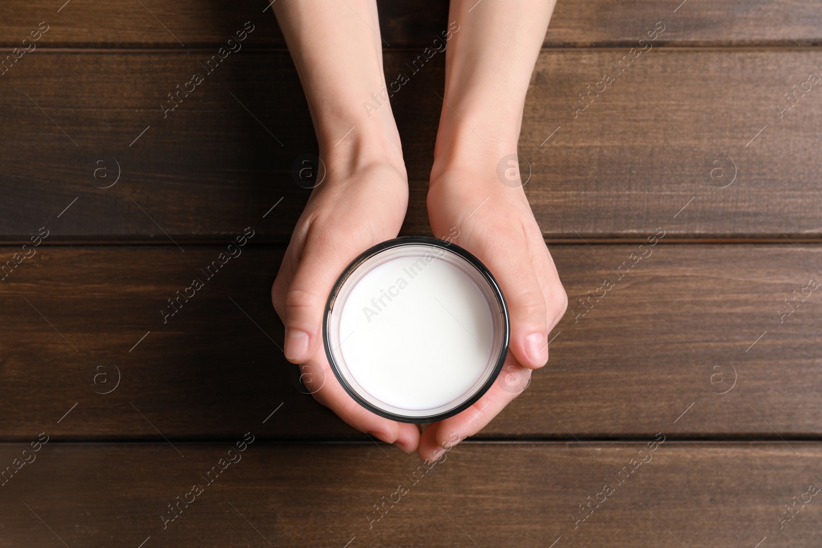 Photo of Woman holding glass of milk at wooden table, top view