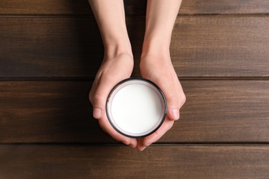 Photo of Woman holding glass of milk at wooden table, top view