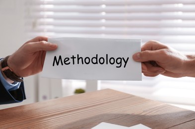 Image of Man giving paper with word Methodology to colleague in office, closeup