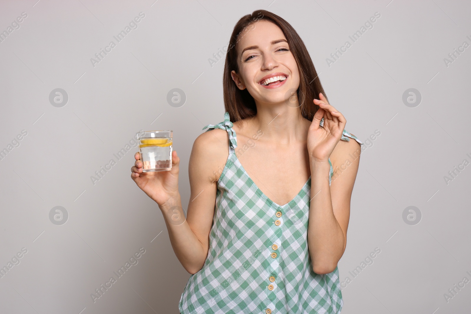 Photo of Young woman with glass of lemon water on light background