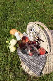 Photo of Picnic basket with tasty food, flowers and cider on grass