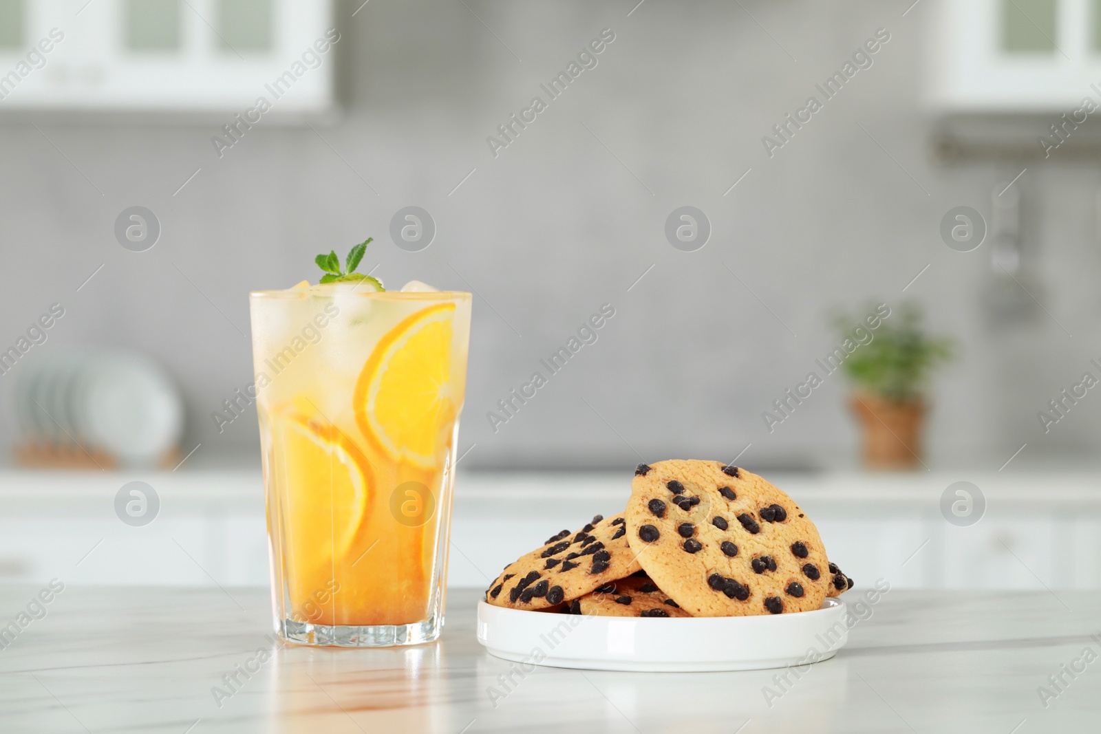 Photo of Tasty refreshing drink with orange and cookies on white marble table in kitchen