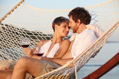Young couple resting with glasses of wine in hammock on beach