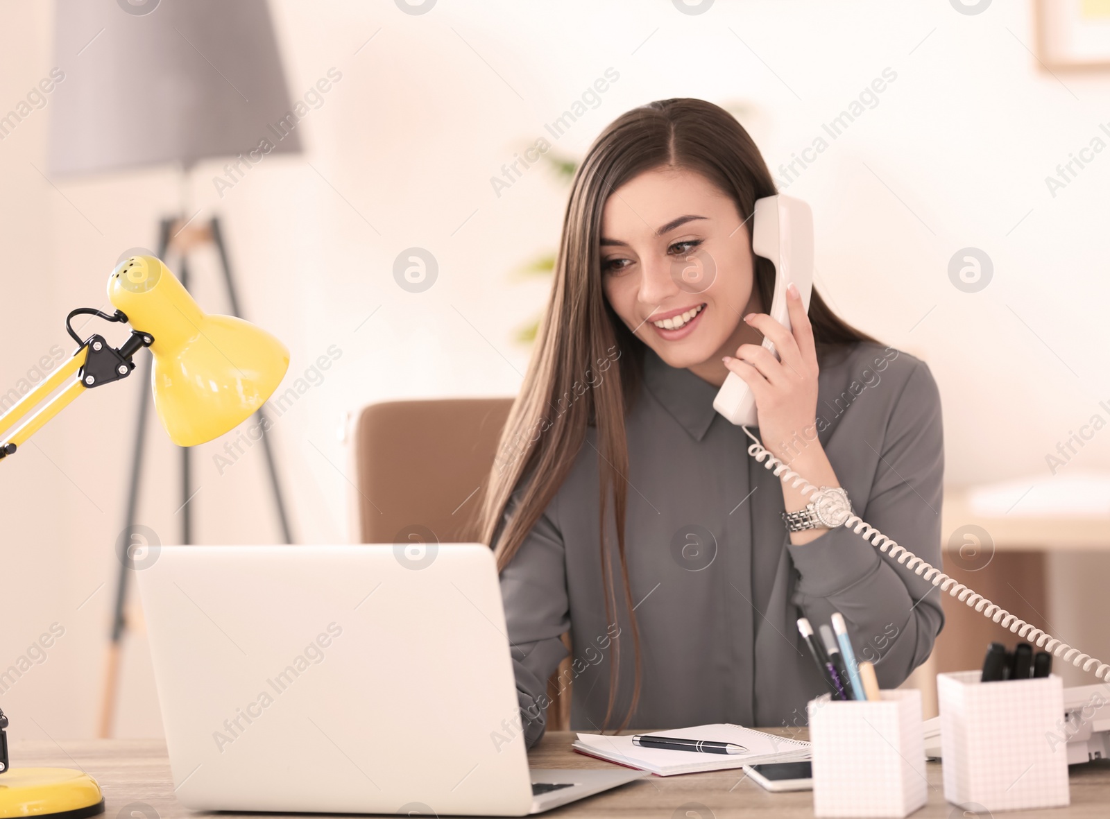 Photo of Young woman talking on phone at workplace