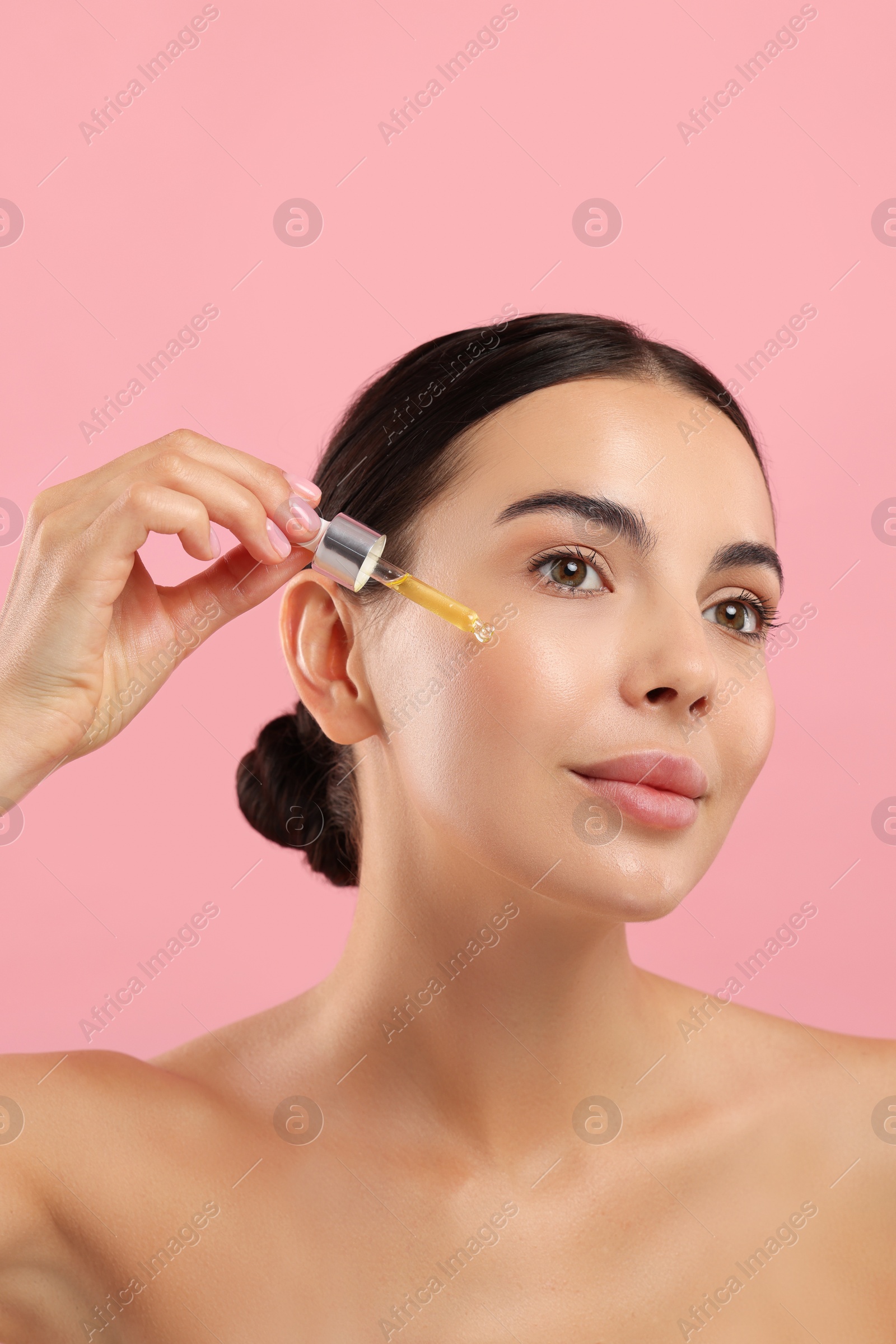 Photo of Beautiful young woman applying serum onto her face on pink background