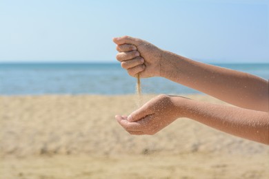 Child pouring sand from hands on beach, closeup. Fleeting time concept