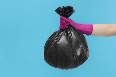 Photo of Woman holding plastic bag full of garbage on light blue background, closeup. Space for text