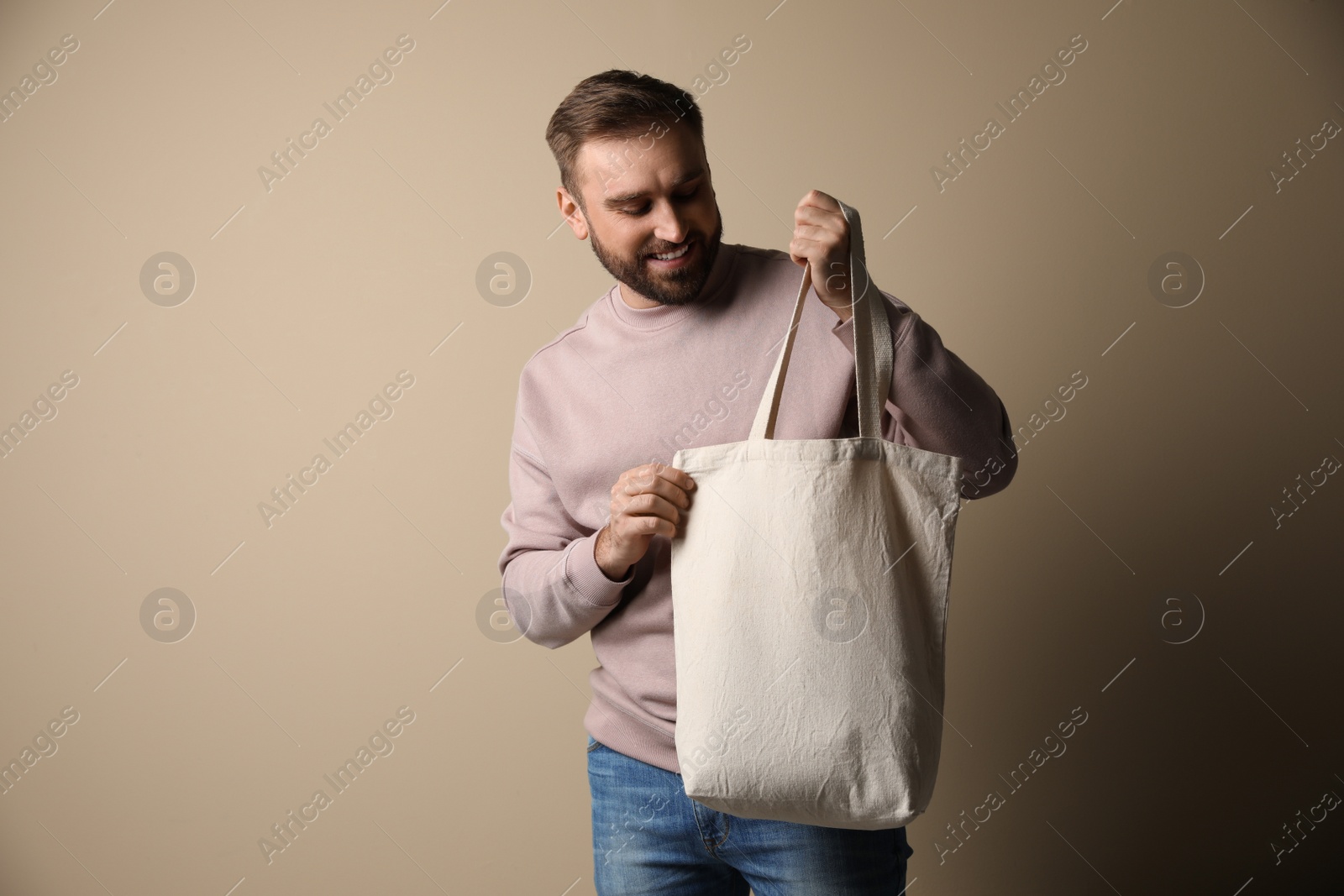 Photo of Happy young man with eco bag on beige background. Space for text