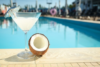 Photo of Tasty refreshing cocktail and coconut on edge of swimming pool. Party items