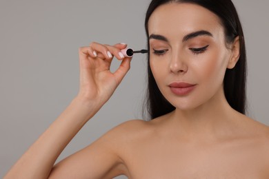 Photo of Beautiful young woman applying mascara on grey background