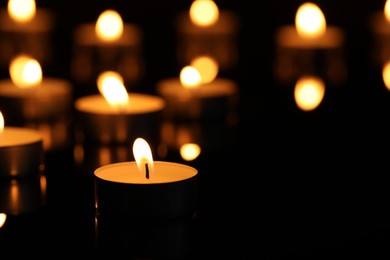 Photo of Burning candles on surface in darkness, closeup. Space for text