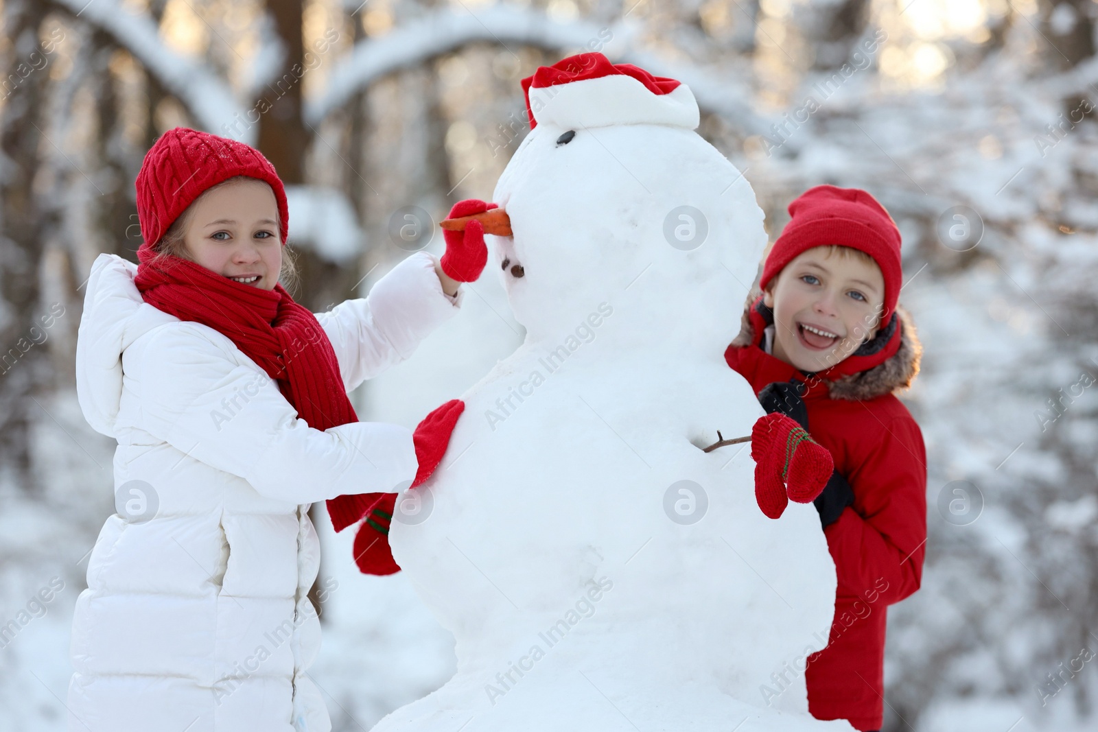 Photo of Cute little girl and boy making snowman in winter park