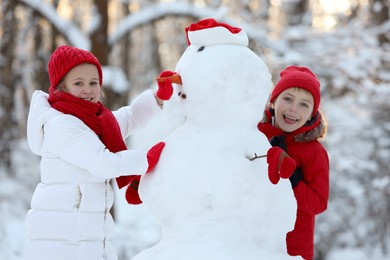 Cute little girl and boy making snowman in winter park
