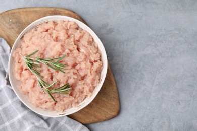 Photo of Fresh raw minced meat and rosemary in bowl on light grey textured table, top view. Space for text