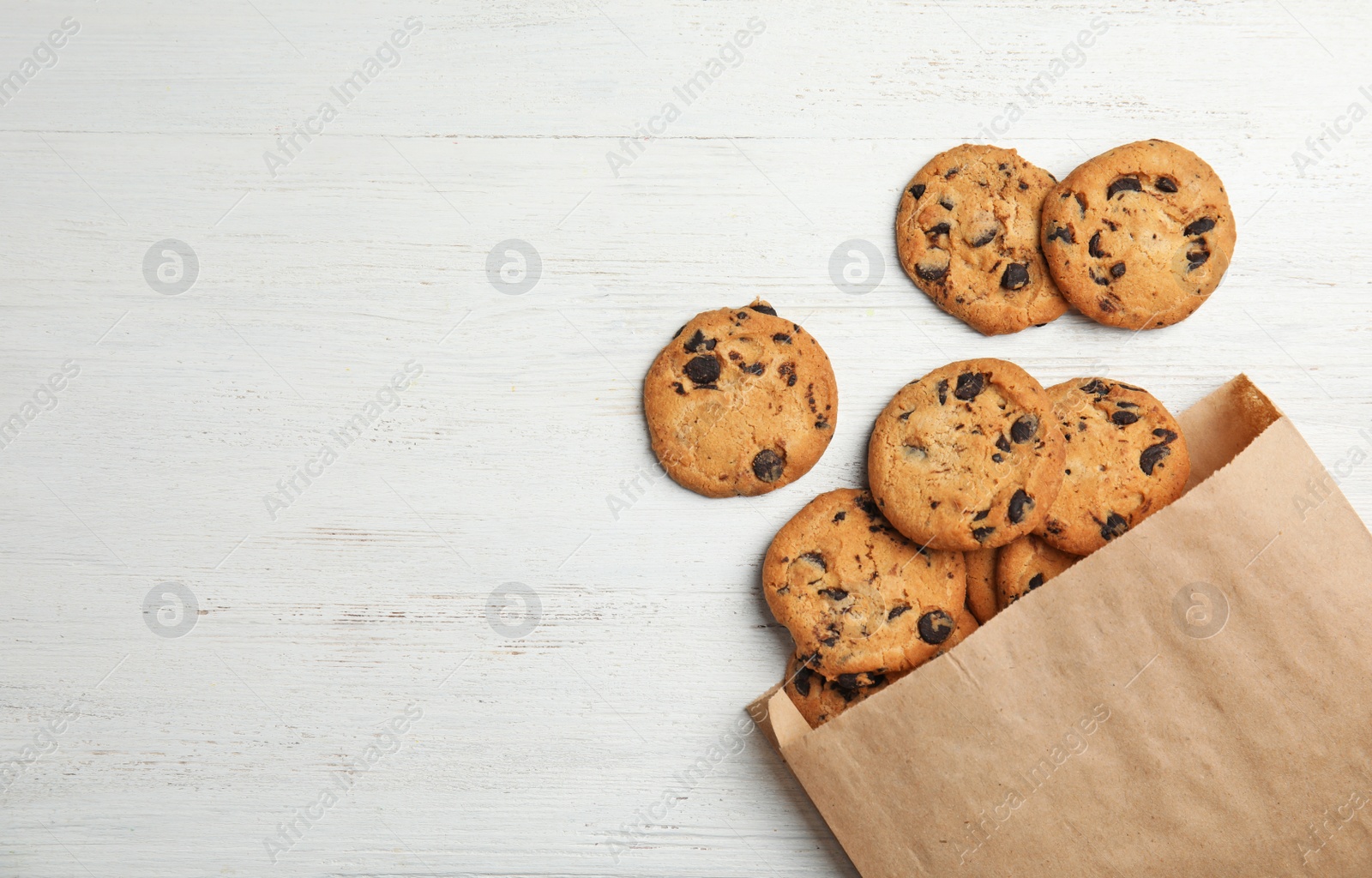 Photo of Paper bag with delicious chocolate chip cookies on wooden table, flat lay. Space for text