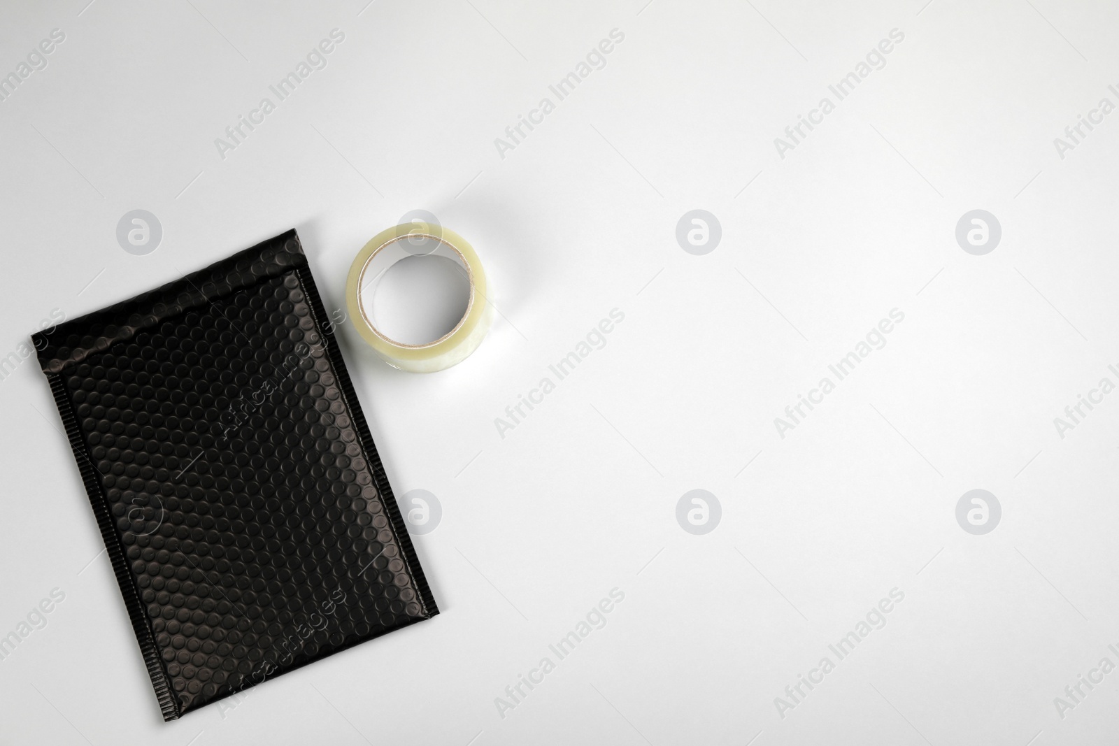 Photo of Padded envelope with bubble wrap and tape on light background, flat lay. Space for text