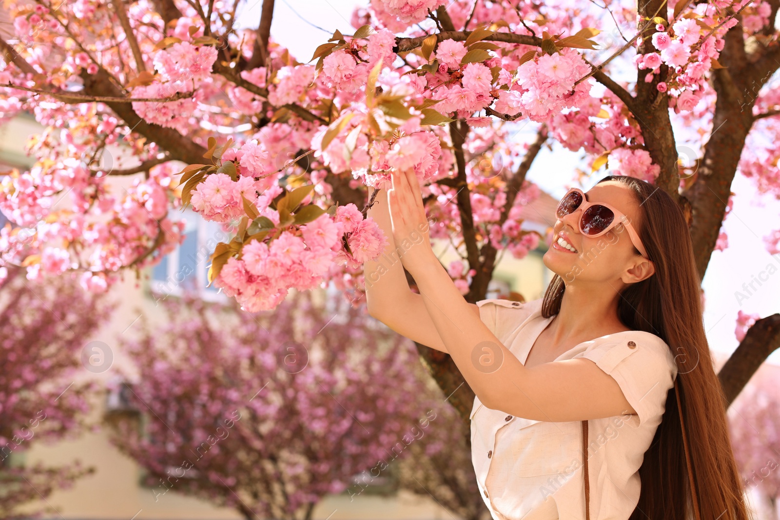 Photo of Happy stylish young woman near blossoming sakura tree outdoors. Spring look