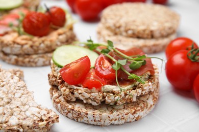 Photo of Crunchy buckwheat cakes with prosciutto, pieces of tomato and cucumber slice on white table, closeup