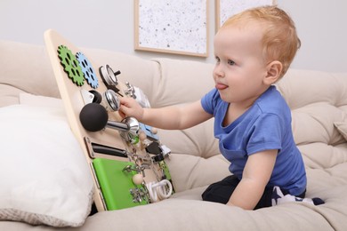 Photo of Cute little boy playing with busy board on sofa at home