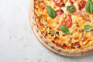 Tasty quiche with cheese, tomatoes and basil leaves on light grey table, top view. Space for text